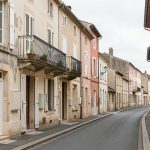 Rue résidentielle du centre-ville de Tonneins avec façades anciennes, volets, balcons et panneaux immobiliers vierges, éclairée par une lumière naturelle douce.