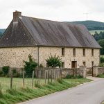 Quelles communes choisir parmi les 15 où louer une maison plutôt qu’acheter dans la Nièvre ? Maison individuelle en pierre située dans une rue calme d’un village rural de la Nièvre, avec le paysage vallonné du Morvan en arrière-plan.