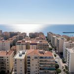 Vue réaliste de Toulon depuis les hauteurs, avec les immeubles du centre-ville et la mer Méditerranée en arrière-plan.